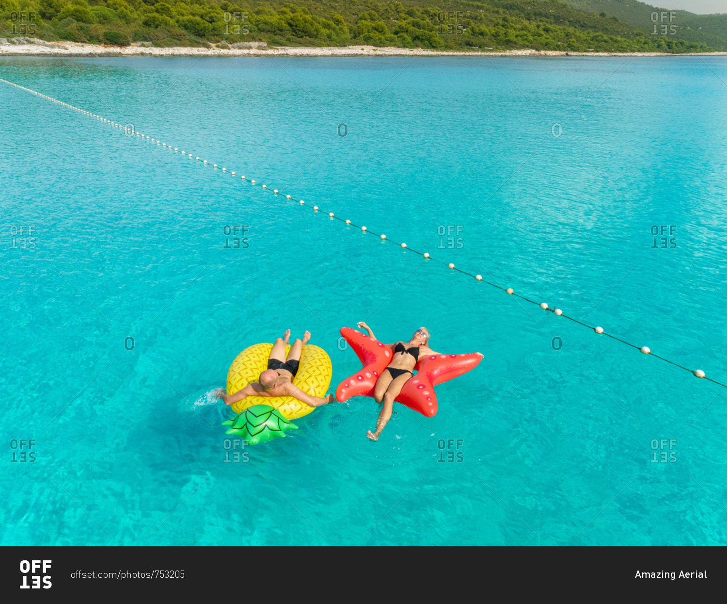 Aerial view of man and woman floating by string buoy on inflatable mattresses in clear blue Adriatic sea.