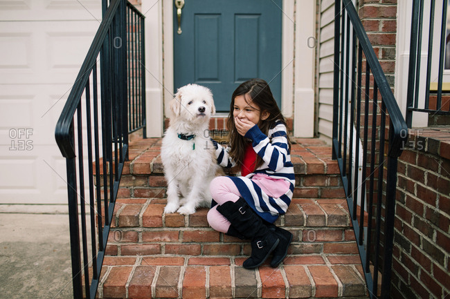 Laughing girl covering her mouth and sitting on front stoop with white dog