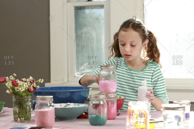 Young girl mixing ingredients in bowl to make slime at home