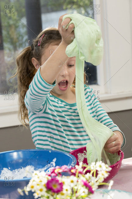 Shocked girl stretching slime from mixing bowl at home