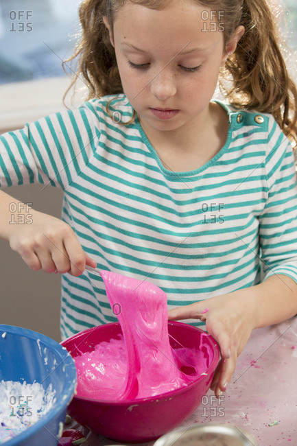 Cute girl mixing pink glitter slime with spoon in bowl at home