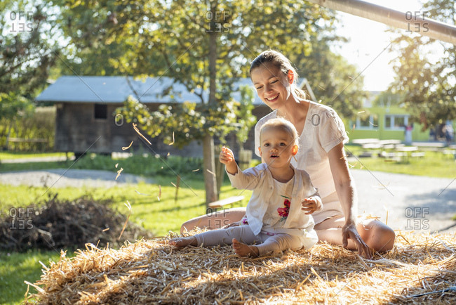 Happy mother and little daughter playing with straw on a farm