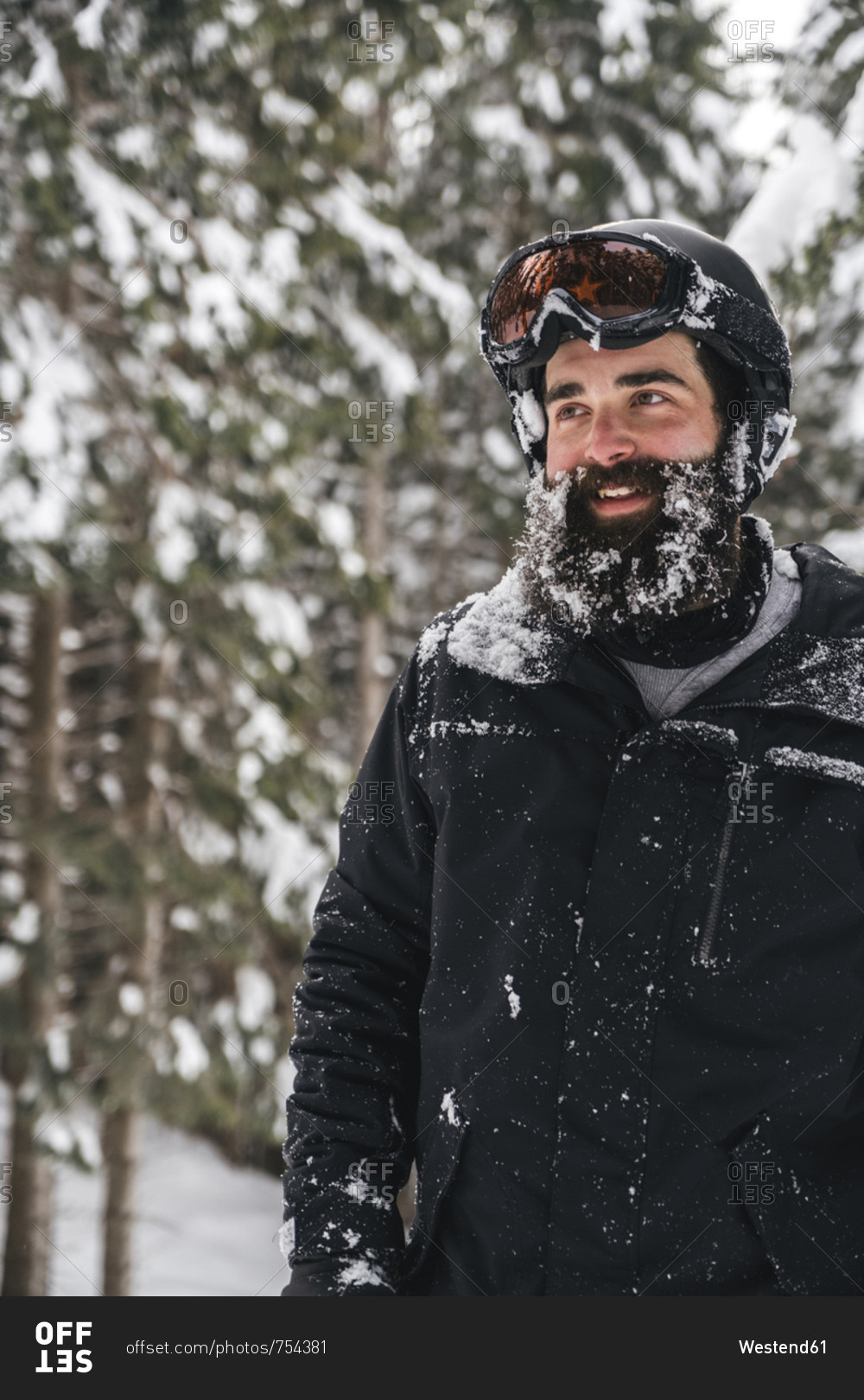 Smiling young man in skiwear in winter forest looking sideways