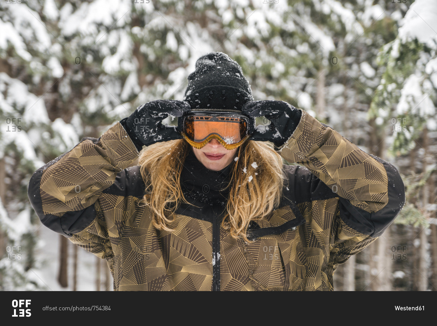 Young woman putting on ski goggles in winter forest