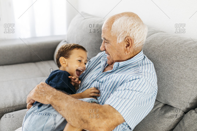 Grandson and grandfather laughing while tickling each other on the couch