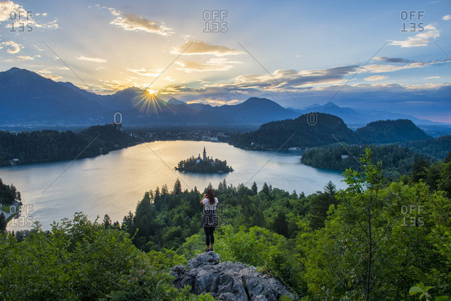 Slovenia- Bled-  Young woman taking picture of Bled island and Church of the Assumption of Maria at sunrise