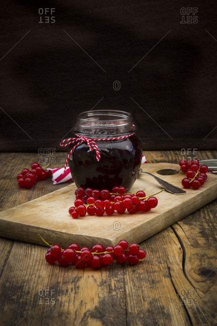 Jam jar of currant jelly and red currants on wooden board