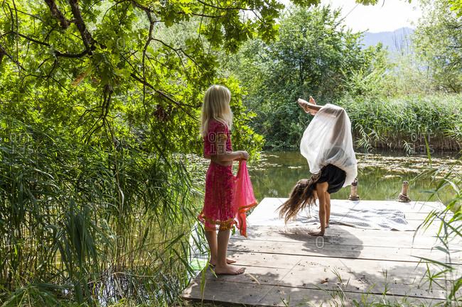 Girl on jetty at a pond watching friend doing a handstand