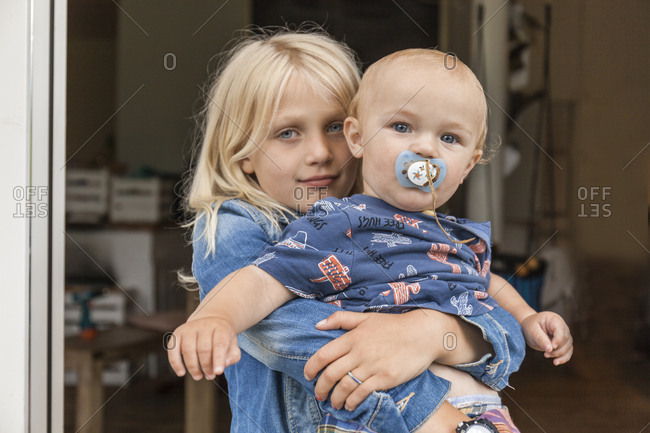 Portrait of girl holding baby boy brother at home