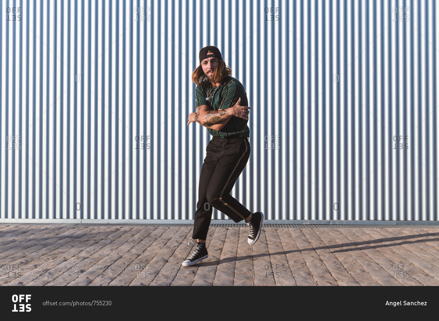 Young man with cap and sports clothes dancing hip hop in the street in a sunny day iron wall background