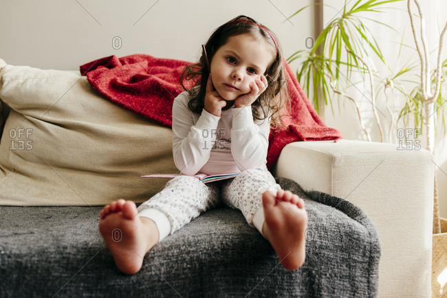 Cute little girl sitting on the couch with a notebook looking for inspiration