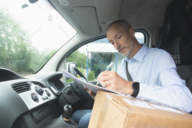 Side view of delivery man writing on paper in delivery van