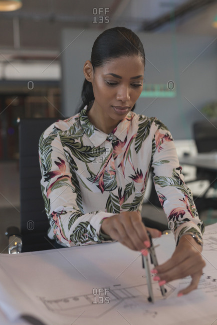 Female executive drawing on blueprint at desk in office
