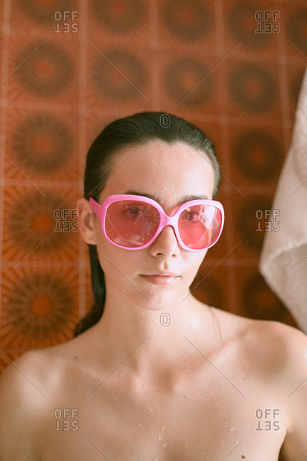 Young brunette woman with pink retro eyeglasses relaxing on bath under neon colorful lights