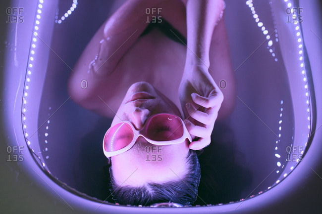 Young brunette woman with pink retro eyeglasses relaxing on bath under neon colorful lights