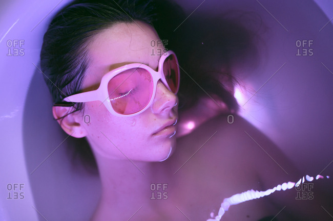 Young brunette woman with pink retro eyeglasses relaxing on bath under neon colorful lights