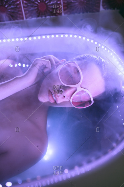 Young brunette woman with pink retro eyeglasses relaxing on bath under neon colorful lights