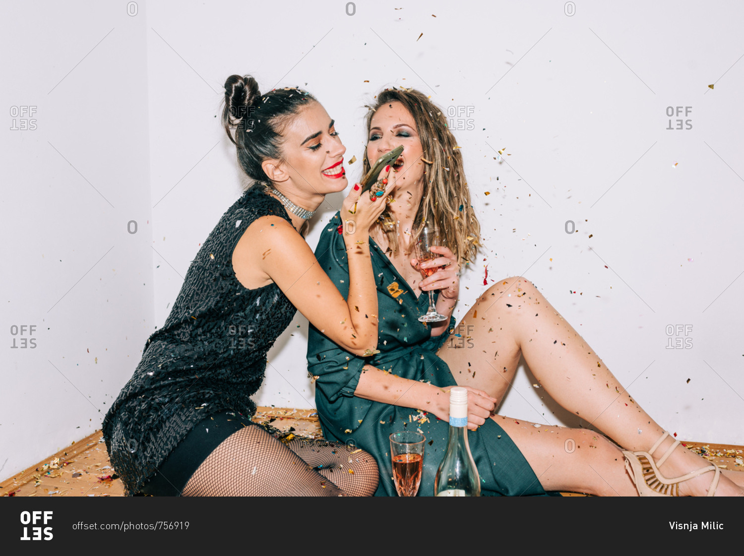 Two dressed up women celebrating New Year's Eve and wishing a happy New Year to someone on the phone