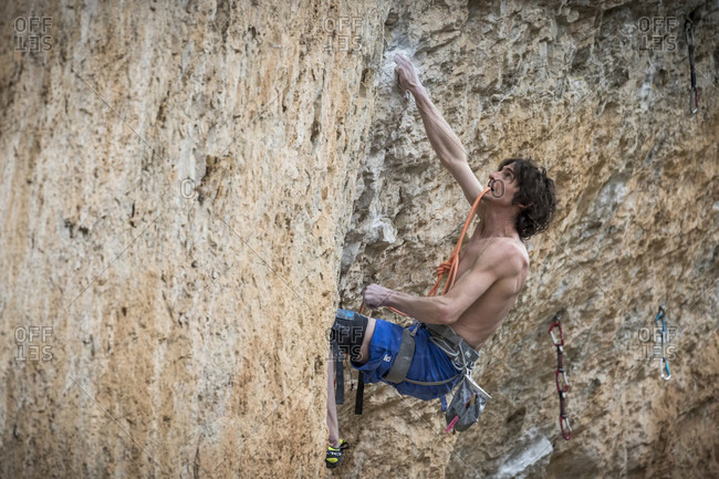 March 4, 2018: Side view of single shirtless rock climber climbing challenging cliff, Siurana, Catalonia, Spain