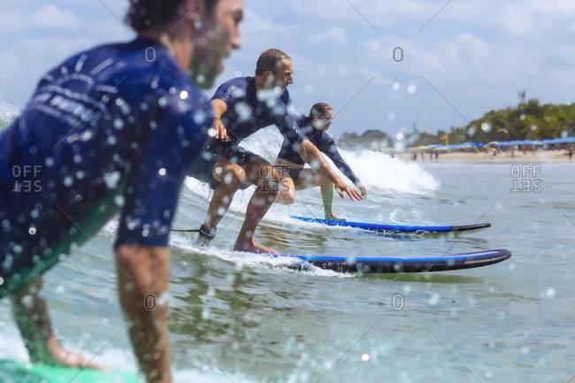 September 18, 2017: Side view of three adventurous surfers riding wave in sea