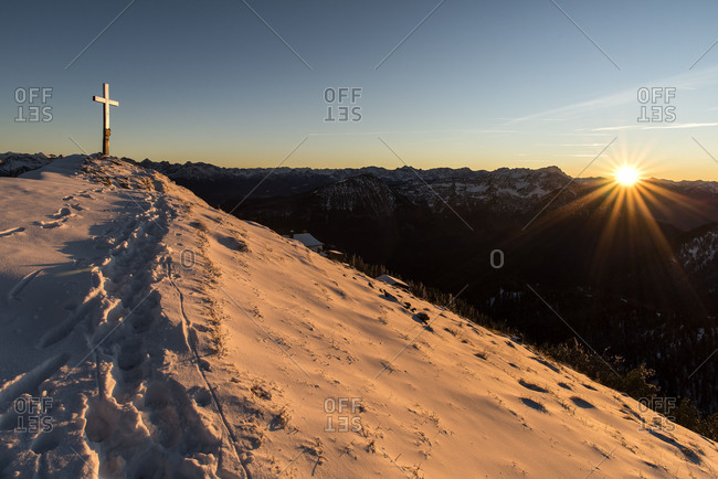 Evening sun at the summit of the Heimgarten, summit cross shines in the snow of the foreground footprints.