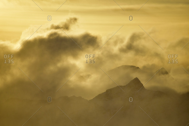 View from the Herzogstand on a sea of clouds and some silhouettes of mountaintops in the golden evening light.