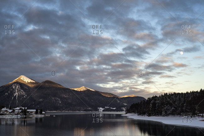 The Jochberg is shone on by the last evening light. Snow covers the village Walchensee and the shore of the Walchensee.