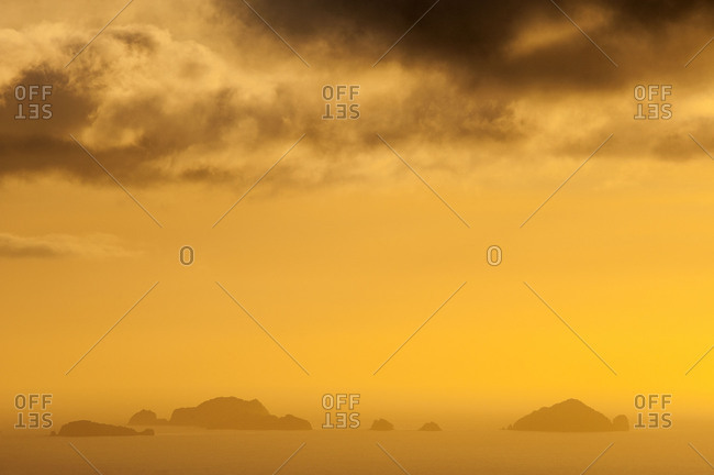 Small islands on the New Zealand coast of Coromandel during a golden light mood with dark clouds.