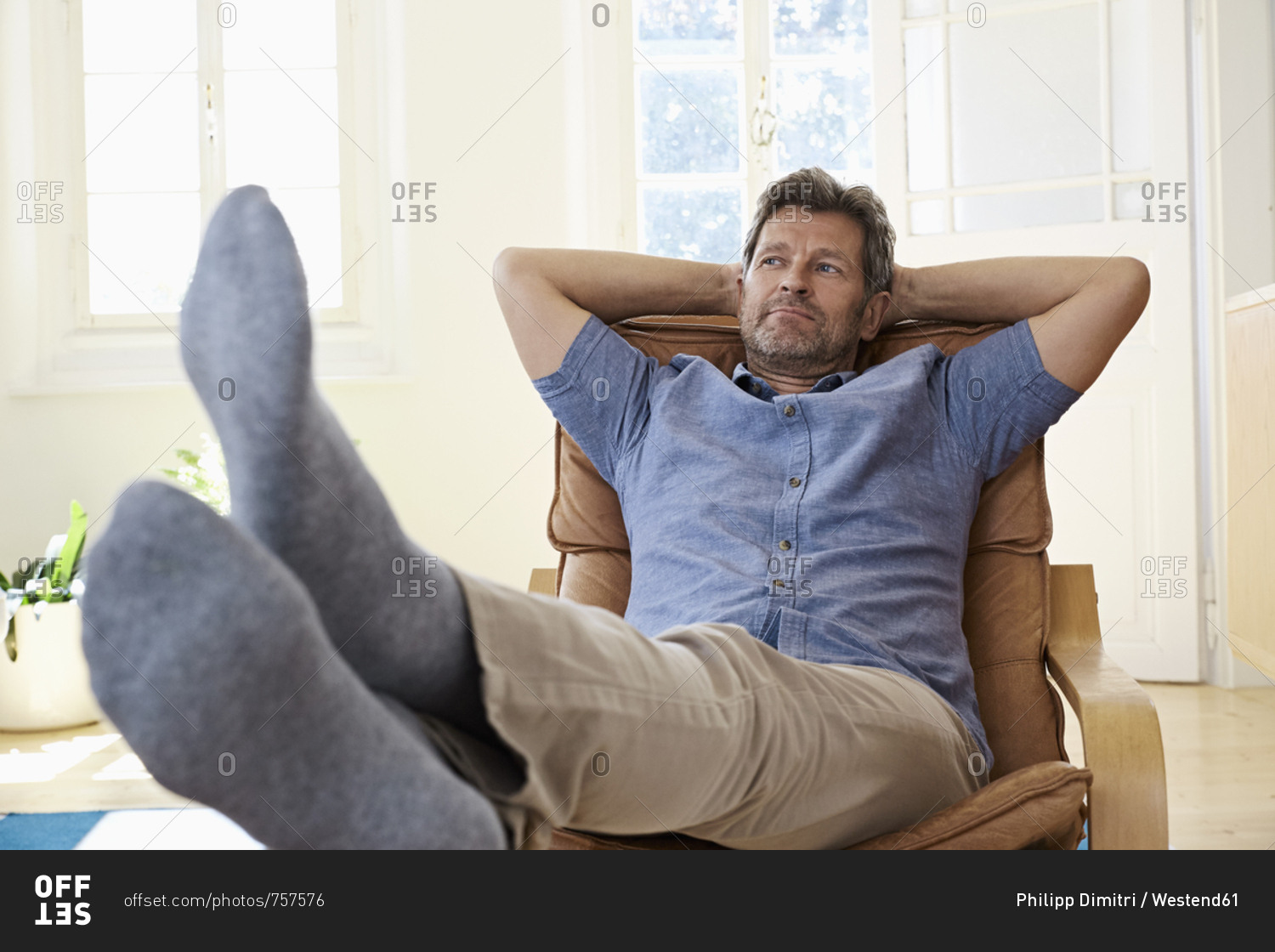 Man sitting in arm chair with feet up- daydreaming stock photo - OFFSET