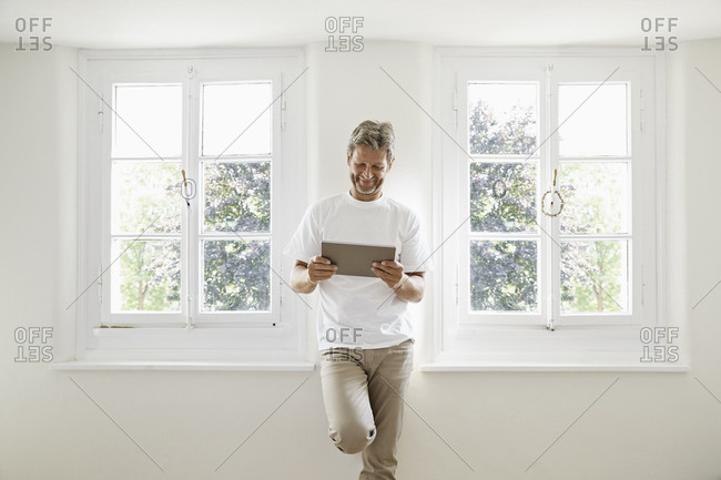 Mature man standing at window using digital tablet 