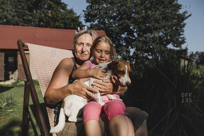 Smiling grandmother with granddaughter and dog on deckchair in garden