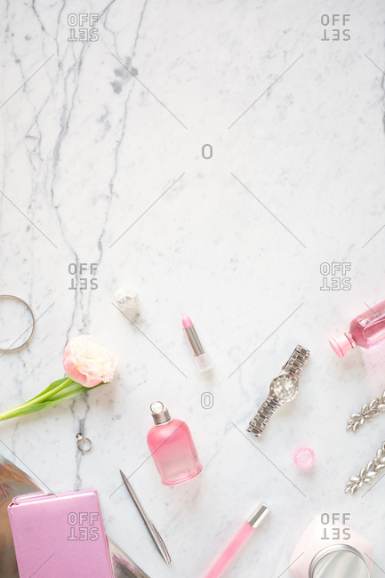 Girly stuff on table. Flat lay composition of perfume, lipstick, wristwatch, pink rose and accessories on white marble table background