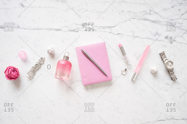 Flat lay with girlish stuff. Creative composition of perfume bottle, lipstick, notebook, pen, wristwatch and accessories on white marble table background