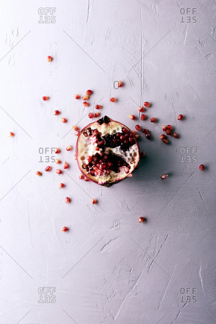 Red fruit inspiration. Directly above view of an opened pomegranate and juicy seeds spread on concrete background
