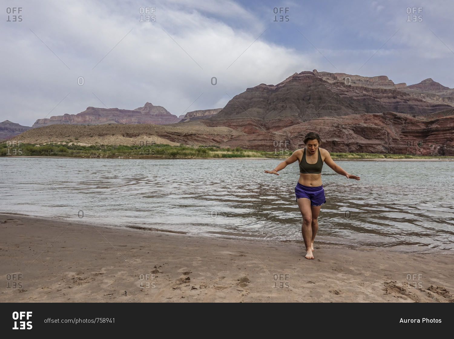 Young woman emerges from cold water of Colorado River after cooling off her feet to celebrate end of long day of hiking, Grand Canyon, Arizona, USA