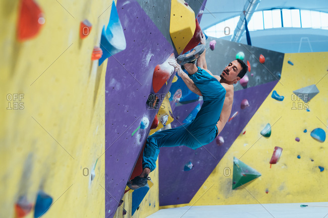 Young man climbing rock wall indoor - healthy lifestyle, sport, climbing concept