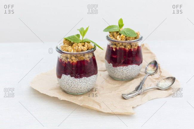 Two glasses of chia pudding with coconut milk- red fruit jelly and peanut granola topping