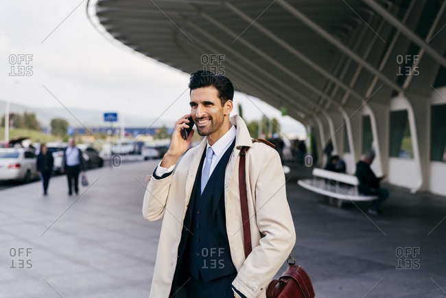 Attractive caucasian businessman with shoulder bag talking on the phone outside the airport terminal