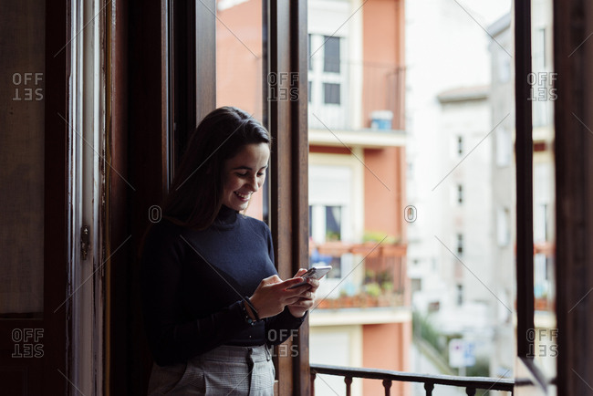 Cute caucasian girl leaning leaning on balcony and using phone at home
