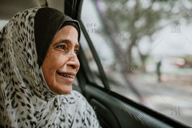 Portrait of smiling Malaysian woman looking out window of car