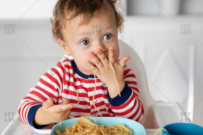 Toddler eating noodles with hands