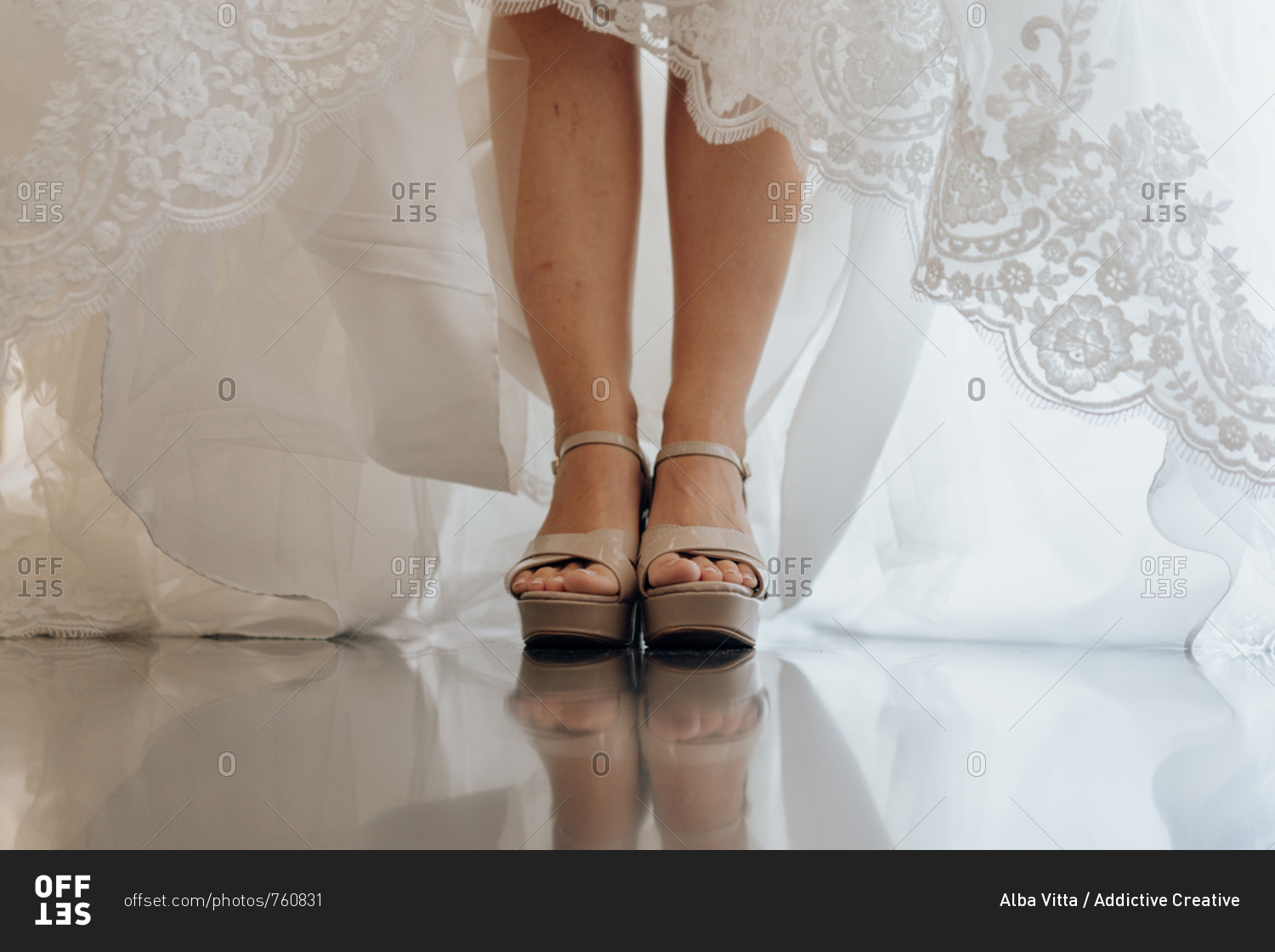 Crop shot of female legs in high heels and bridal white lace dress standing on shiny floor