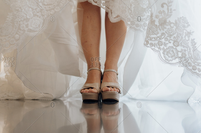 Crop shot of female legs in high heels and bridal white lace dress standing on shiny floor