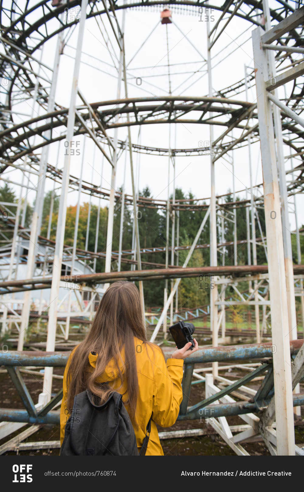 Back view of blond woman with camera taking photo of desolated amusement park with attractions