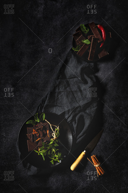 Chocolate with red chili peppers, mint and raspberries on dark background. Flat lay