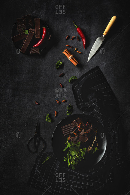 Chocolate with red chili peppers, mint and raspberries on dark background. Flat lay