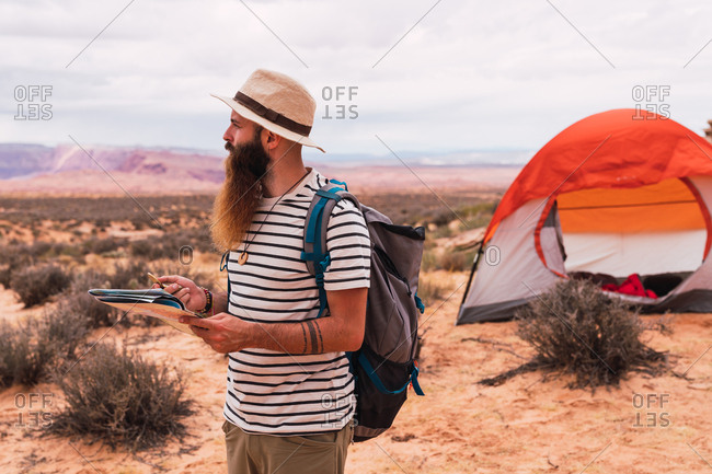 man holding map and retro compass while standing on blurred background of majestic desert
