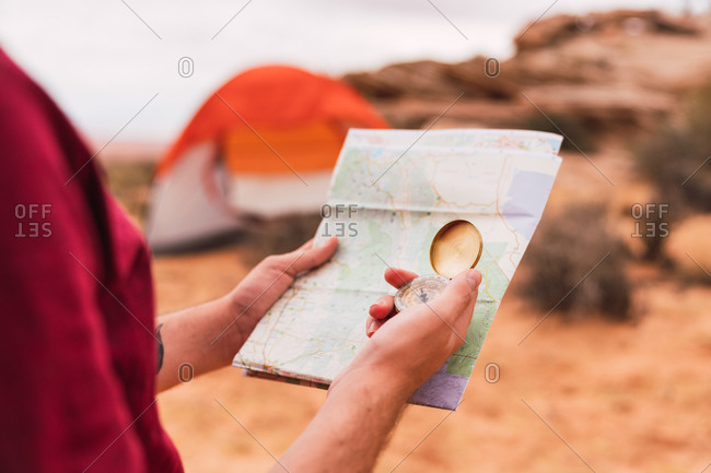 Crop man holding map and retro compass while standing on blurred background of majestic desert