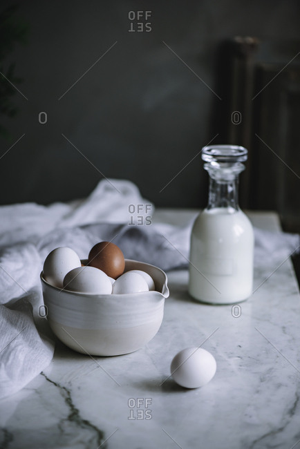 Bowl of chicken eggs and bottle of fresh dairy standing on marble tabletop in kitchen