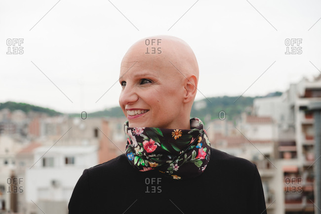 Bald woman standing on rooftop with city behind